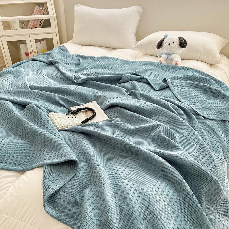 Plaid en coton gaufré bleu lac posé sur un lit